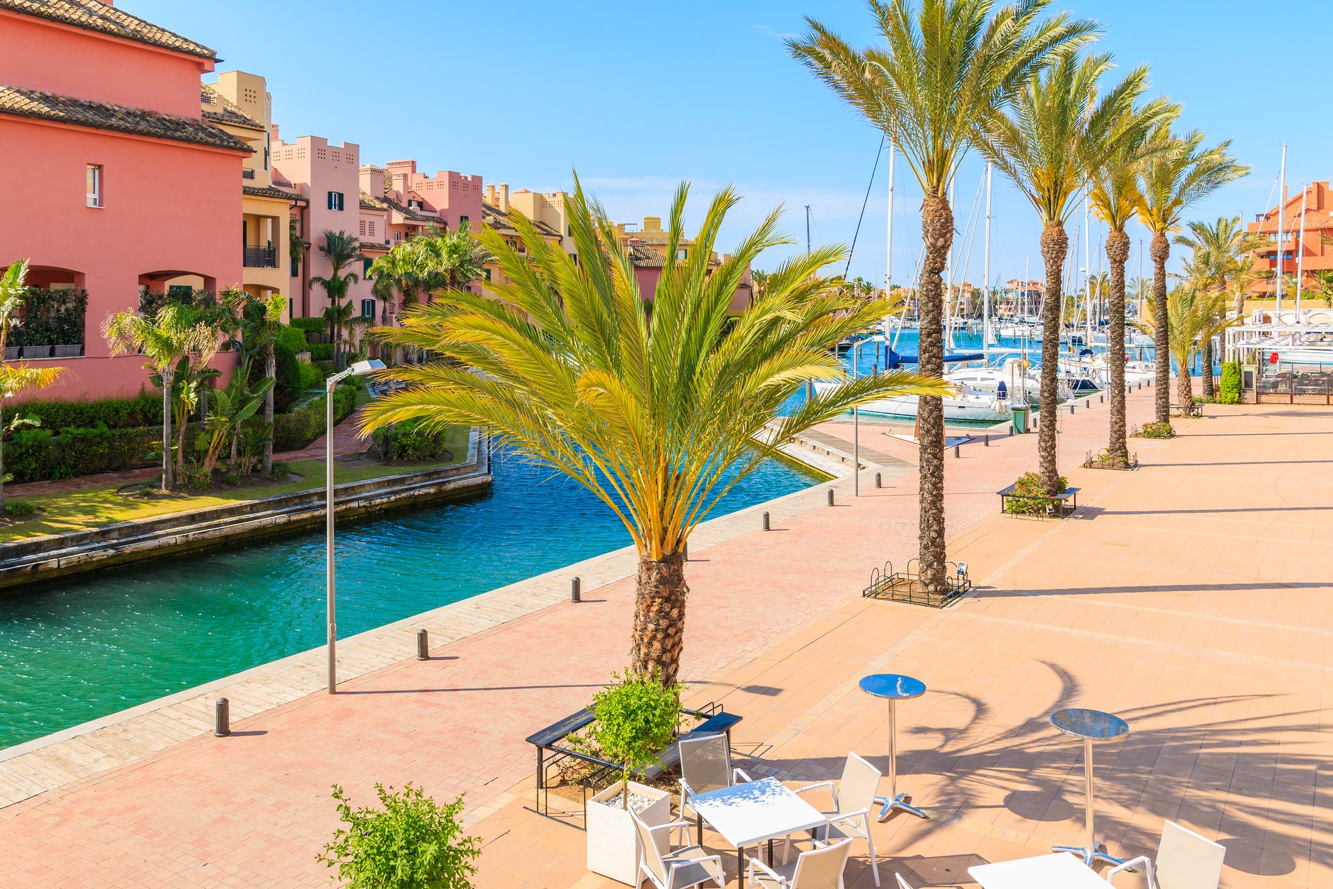 Pink building with palm trees, marina view, outdoor seating area.